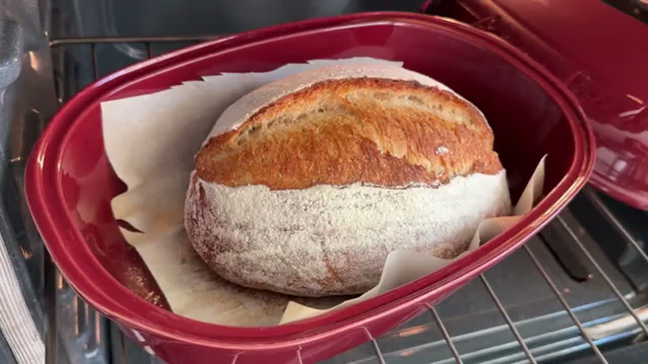 A finished artisan loaf with a golden crust inside a red bread baker