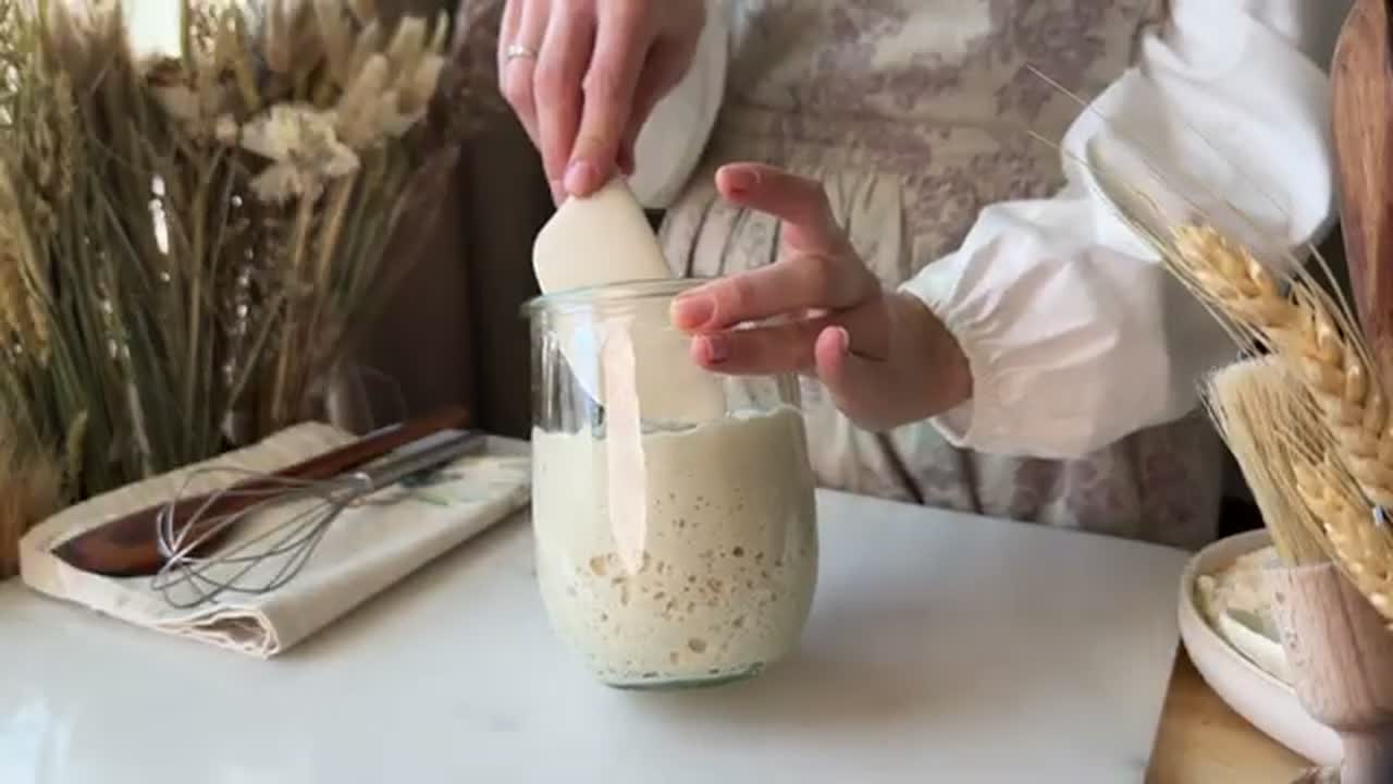 Active sourdough starter in a glass jar being stirred